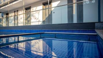 A swimming pool with clear blue tiles, a glass railing, and a building with windows in the background.