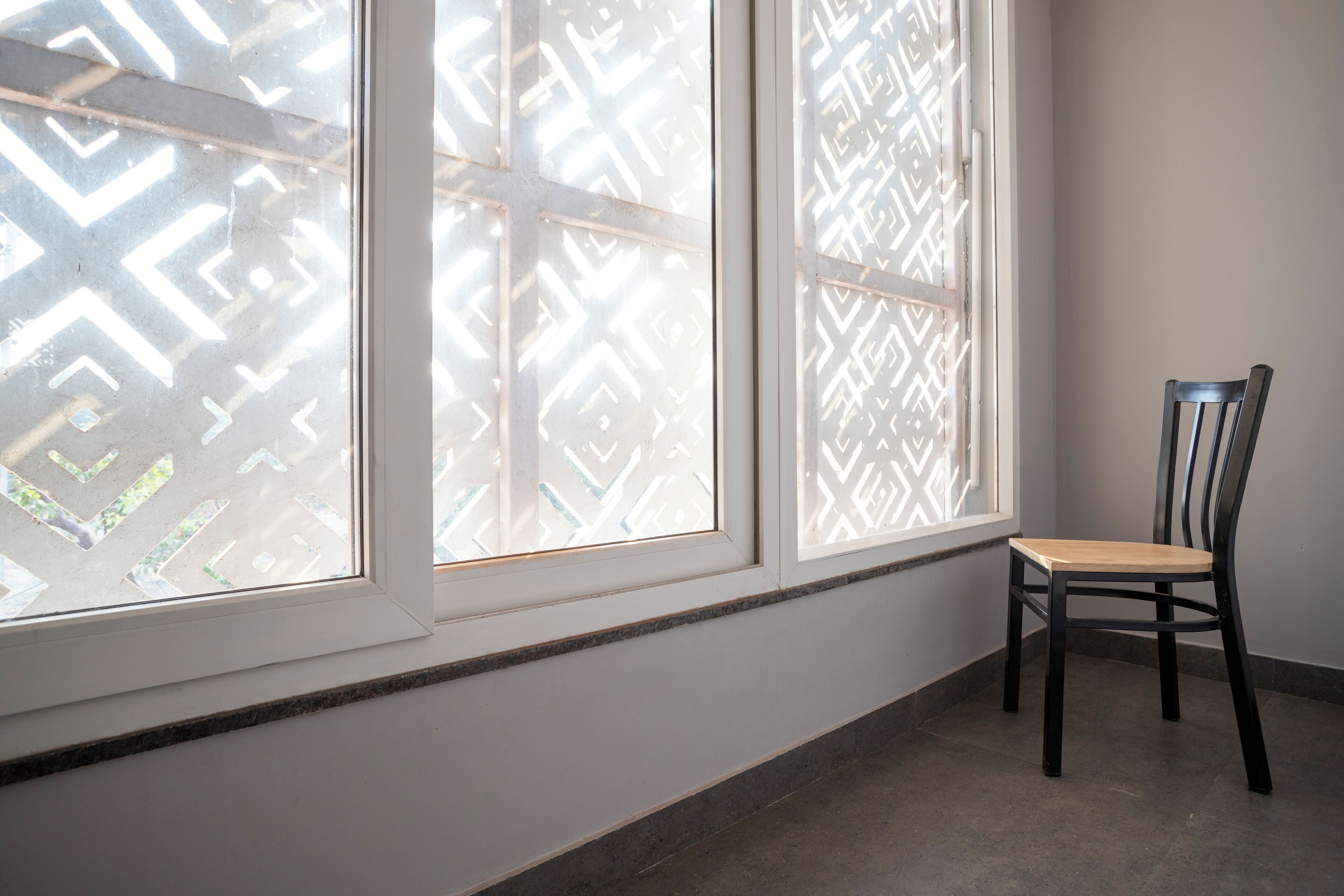 A room with a window, a chair, and a patterned window blind.