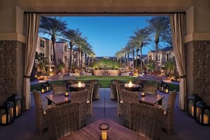 An outdoor dining area with wicker furniture and candles, overlooking a well-maintained lawn and buildings. - Always a Great Idea To Unwind! Close to Portalis Office Park, w/ Outdoor Pool! (Scottsdale)
