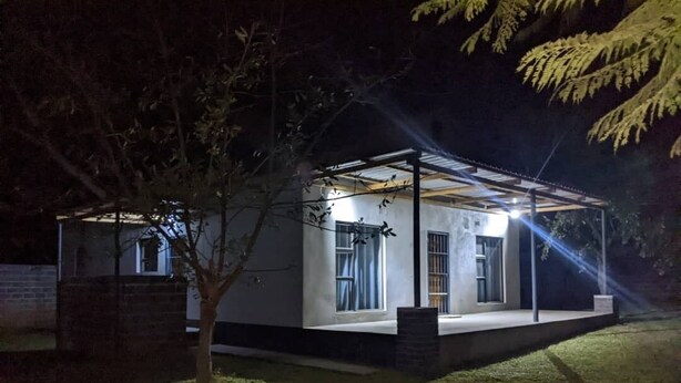 Ein modernes Haus mit überdachter Veranda, einem kleinen Baum und stimmungsvoller Außenbeleuchtung bei Nacht.