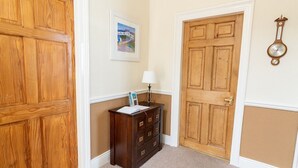 Een hal met houten deuren, een klein houten dressoir met een lamp, en een lijst met een foto aan de muur.