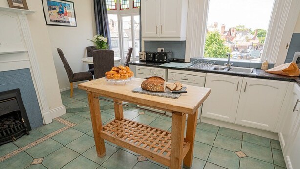 Een keuken met een houten tafel, een open haard en uitzicht op de straat.