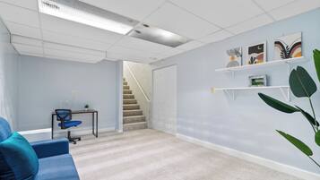 A modern office space with a blue sofa, a desk with a chair, a staircase, and wall art.