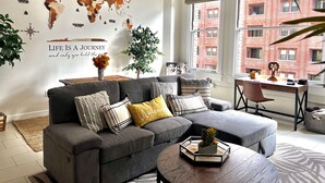 A modern living room with a sectional sofa, a coffee table, and a world map mural on the wall. - Iconic Heart of DTLA Loft with Rooftop Pool/Jacuzzi/Skyline (Los Angeles)