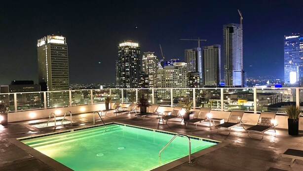 A rooftop pool area with lounge chairs and a view of the city skyline at night. - Iconic Heart of DTLA Loft with Rooftop Pool/Jacuzzi/Skyline (Los Angeles)