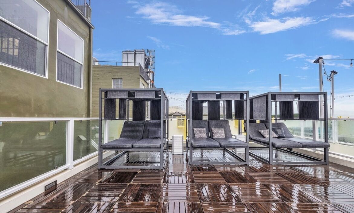 A rooftop terrace with four lounge chairs and a wooden deck.