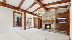 Un dormitorio con una cama grande, una chimenea de piedra, vigas de madera y un televisor montado en la pared.