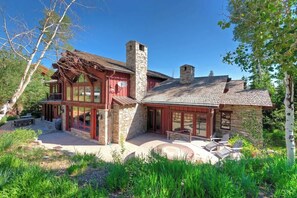 Une maison à deux étages avec une cheminée en pierre, de grandes fenêtres et un patio doté de meubles d’extérieur.