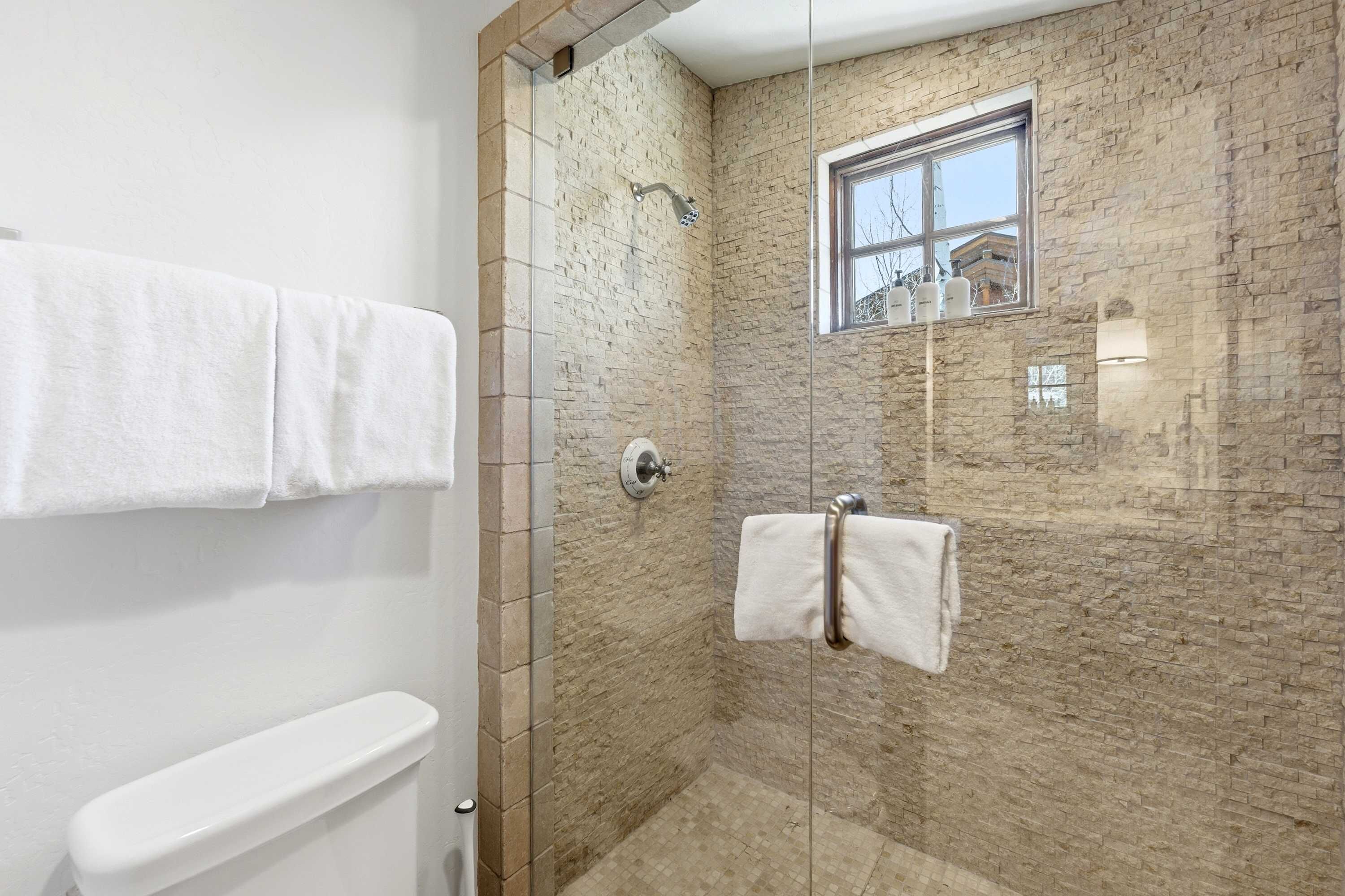 A bathroom with a glass-enclosed shower, a window, and a towel rack.