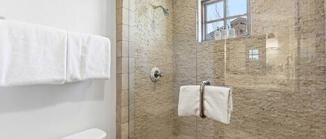 A bathroom with a glass-enclosed shower, a window, and a towel rack.