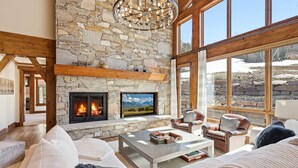 Un salón amplio con chimenea de piedra, asientos cómodos y ventanas grandes.
