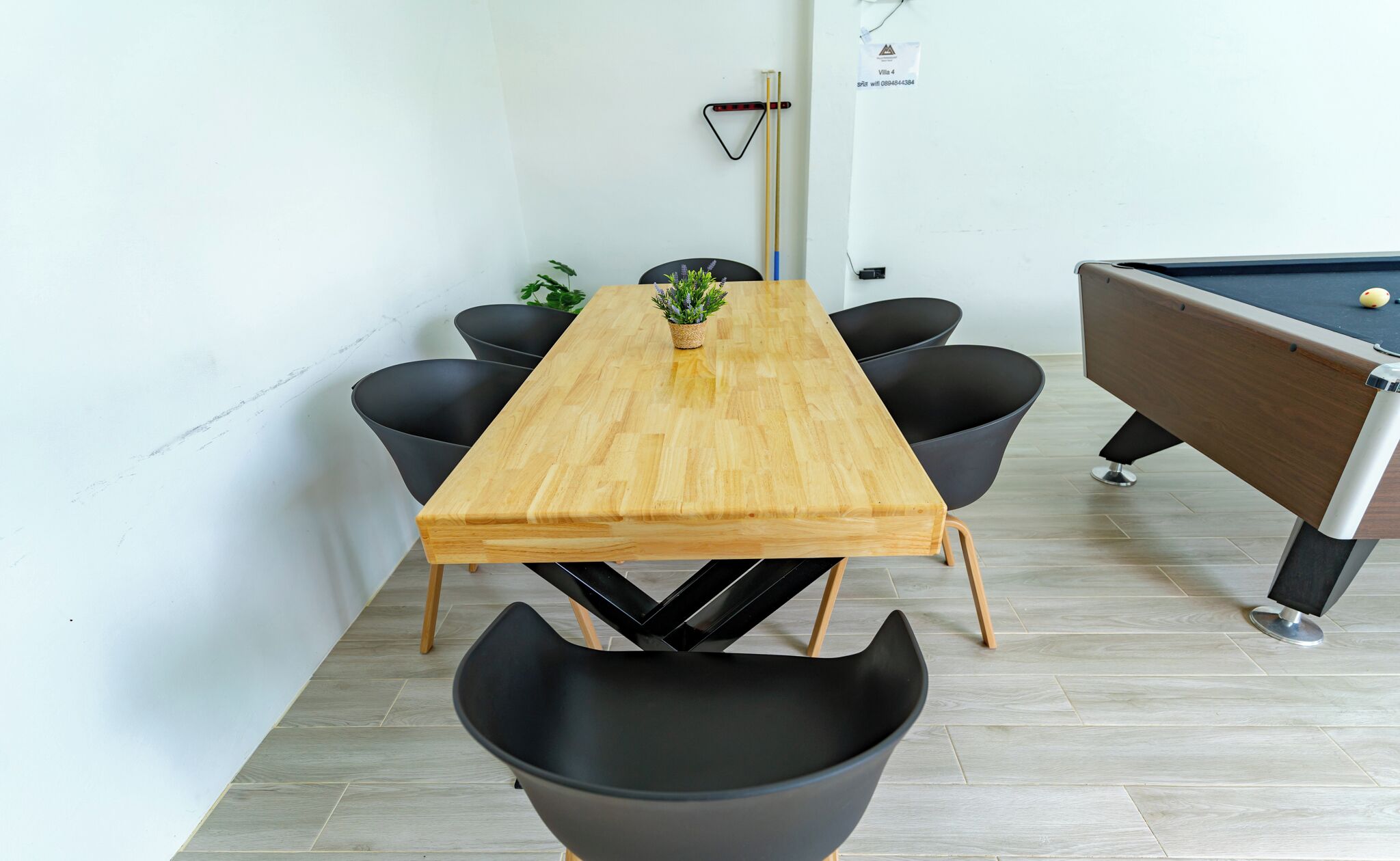 Una mesa rectangular de madera con cuatro sillas negras, una mesa de billar y una planta en maceta sobre la mesa.