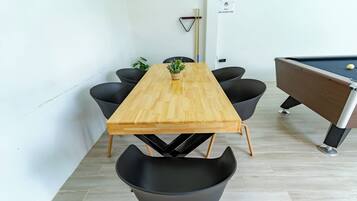 Una mesa rectangular de madera con cuatro sillas negras, una mesa de billar y una planta en maceta sobre la mesa.
