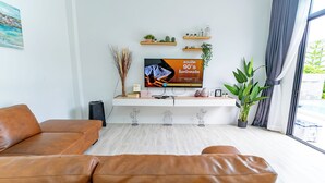 Una sala de estar moderna con un sofá de cuero, un televisor de pantalla plana y un mueble consola minimalista con objetos decorativos y plantas.