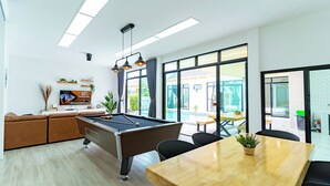 Un espacio interior moderno con mesa de billar, asientos cómodos y ventanas amplias que ofrecen vistas al exterior.