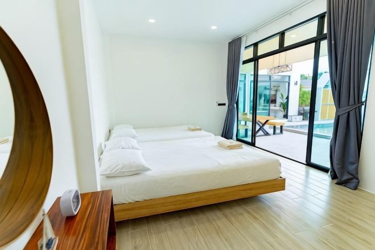 Una habitación de hotel moderna con una cama grande, una mesita de noche de madera y vistas al exterior a través de amplias ventanas.