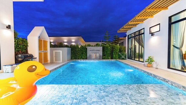 Piscina exterior moderna con caída de agua, rodeada de un jardín ajardinado y una casa contemporánea.