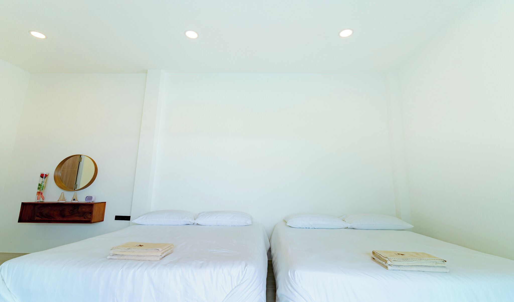 Habitación de hotel con dos camas individuales, un aparador de madera, un espejo redondo y un pequeño estante con objetos decorativos.