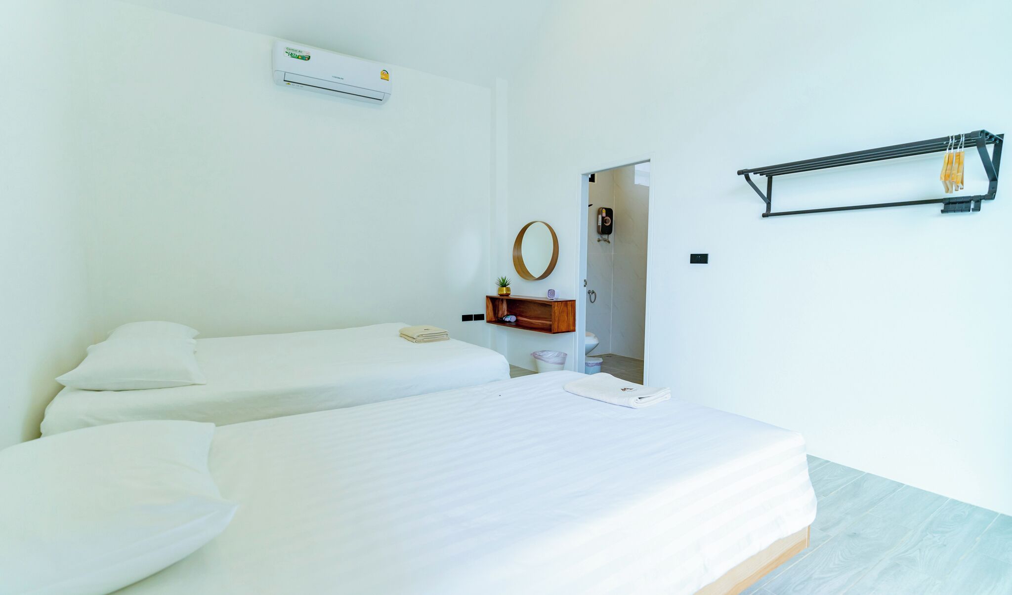 Habitación de hotel con dos camas individuales, un pequeño estante de madera con artículos de aseo, aire acondicionado instalado en la pared y un perchero para toallas.