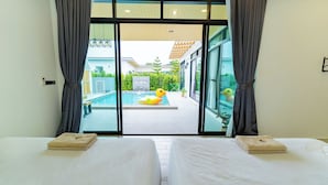 Habitación de hotel con dos camas, vista a una piscina con un flotador de pato y un espacio exterior cubierto.