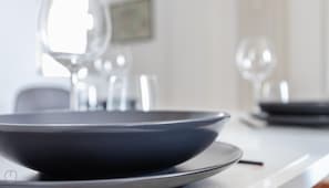 A modern dining area with a dark-colored bowl on a plate, a wine glass, and a blurred background suggesting a bright, well-lit space.