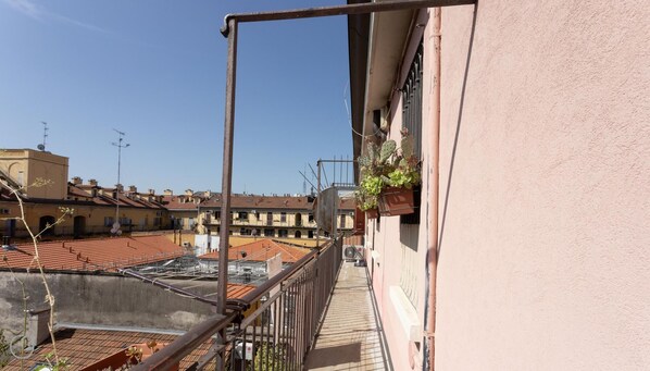 A balcony with a view of a cityscape, including buildings with red-tiled roofs and a clear blue sky.