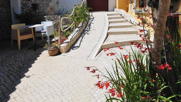 A courtyard with a stone wall, a wooden bench, a table with chairs, and a staircase leading to a door. - Cottage with 2 bedrooms with both en-suite bathrooms in a seaside village (Salir do Porto)