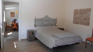A bedroom with a bed, a nightstand, a chair, a table with a vase, and a painting on the wall. - Cottage with 2 bedrooms with both en-suite bathrooms in a seaside village (Salir do Porto)