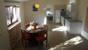 A dining area with a table set for four, a kitchen with a refrigerator and microwave, and a window with blinds. - Cottage with 2 bedrooms with both en-suite bathrooms in a seaside village (Salir do Porto)