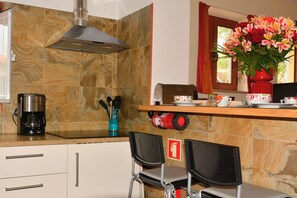 A kitchen with a coffee maker, chairs, a fire extinguisher, and a window with curtains.