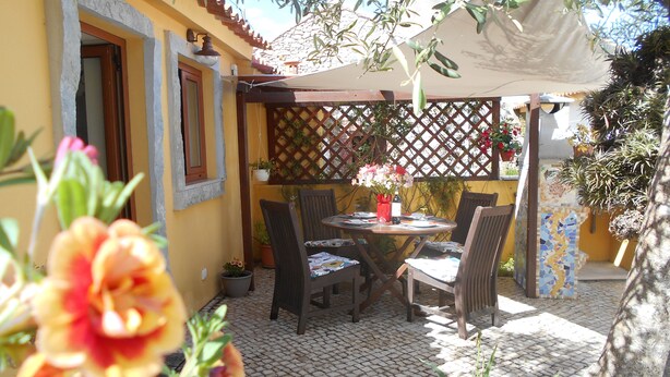 En udendørs terrasse med et bord og stole, omgivet af plantekasser og en espalierstruktur.