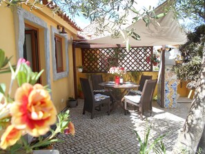 Une terrasse extérieure avec une table et des chaises, entourée de plantes en pot et d’une structure en treillis.