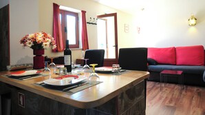 En spiseplads med et træbord dækket til to personer, en vase med blomster og en rød sofa i baggrunden.