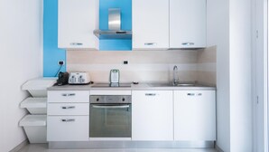 A compact kitchen with white cabinets, a stainless steel range hood, a built-in oven, and a sink.