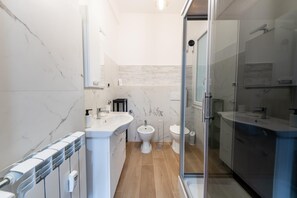 Uma casa de banho moderna com cabine de duche em vidro, uma sanita e uma pia branca.