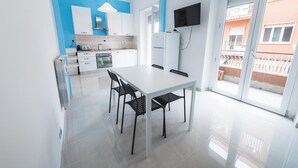 A modern kitchen with white cabinets, a dining table with chairs, and a TV mounted on the wall.