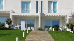 A modern hotel with a stone pathway leading to a double door entrance, white outdoor furniture, and a clear view of the surrounding landscape. - Stunning Capo Falcone Charming Apartments nui0407h (Stintino)