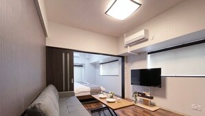 A modern living room with a sofa, a coffee table, a flat-screen TV, and a wooden floor. - Modern 1Br Apt near Hondori District for 6ppl (Naka Ward, Hiroshima)