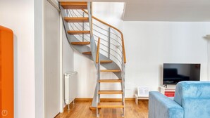 Ein modernes Wohnzimmer mit Wendeltreppe, Heizkörper, Fernseher und einem blauen Sofa.
