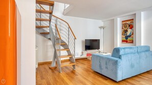 Ein modernes Wohnzimmer mit Wendeltreppe, Flachbildfernseher und blauem Sofa.