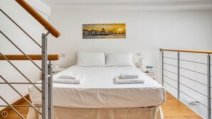 Ein Hotelzimmer mit Bett, weißen Leinentüchern, einem Stadtbildgemälde, einem Nachttisch und Holzboden.