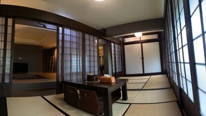 A traditional Japanese room with tatami flooring, a low table with a cushion, and sliding doors.