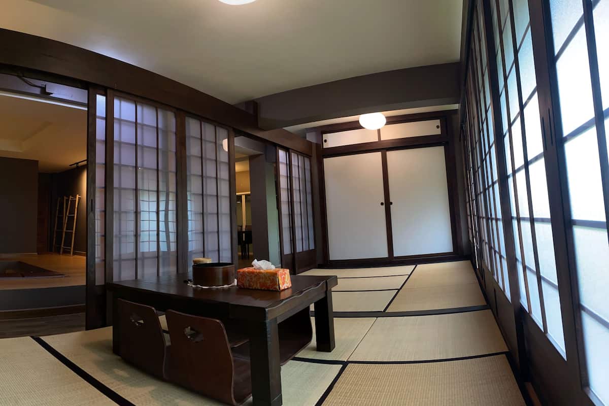 A traditional Japanese room with tatami flooring, a low table with a cushion, and sliding doors.