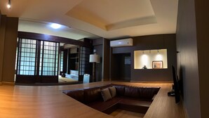A modern living room with a wooden floor, a leather sofa, a TV, and a wall-mounted shelf with framed pictures.