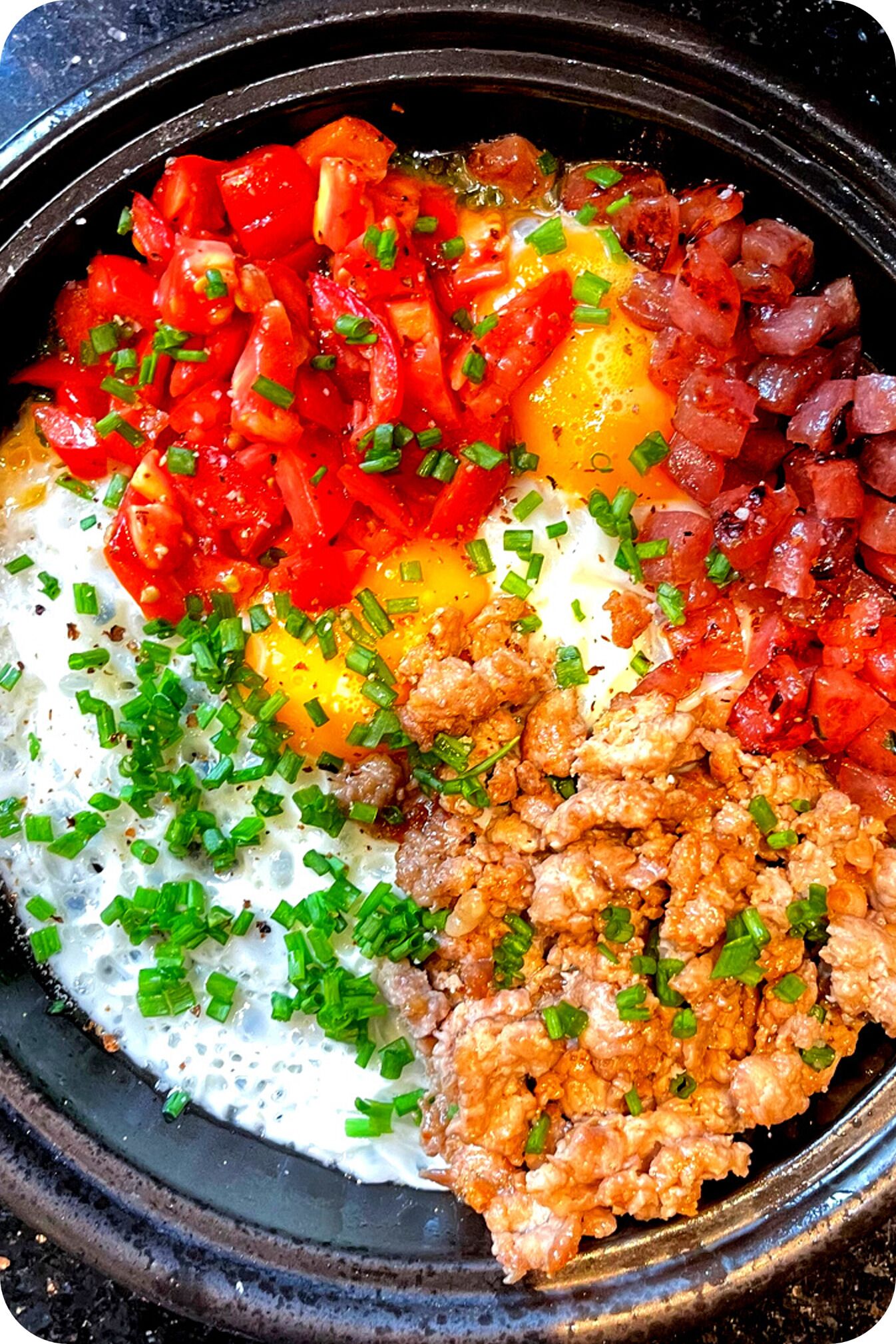 Un plato de desayuno con huevos, tomates, cebollas y cebollines.