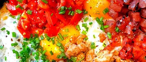 Un plato de desayuno con huevos, tomates, cebollas y cebollines.