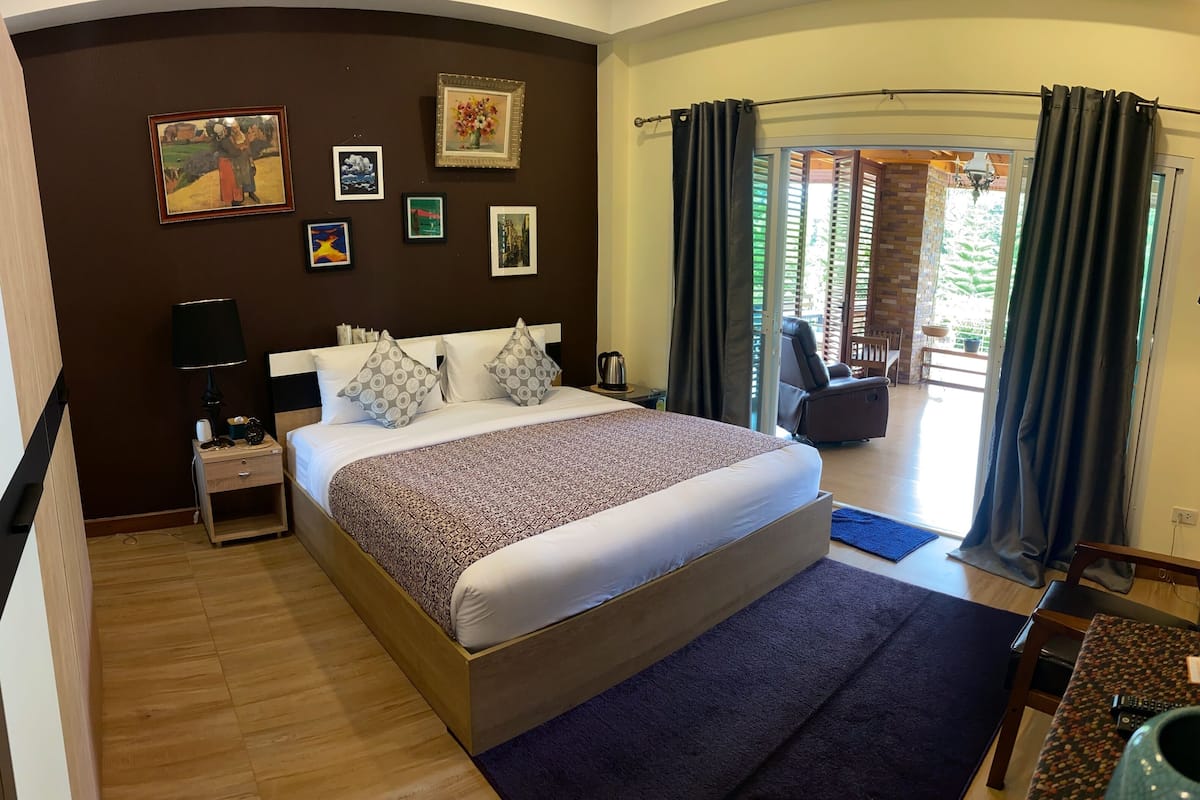A hotel room with a large bed, a nightstand, a lamp, and a wall with framed pictures.