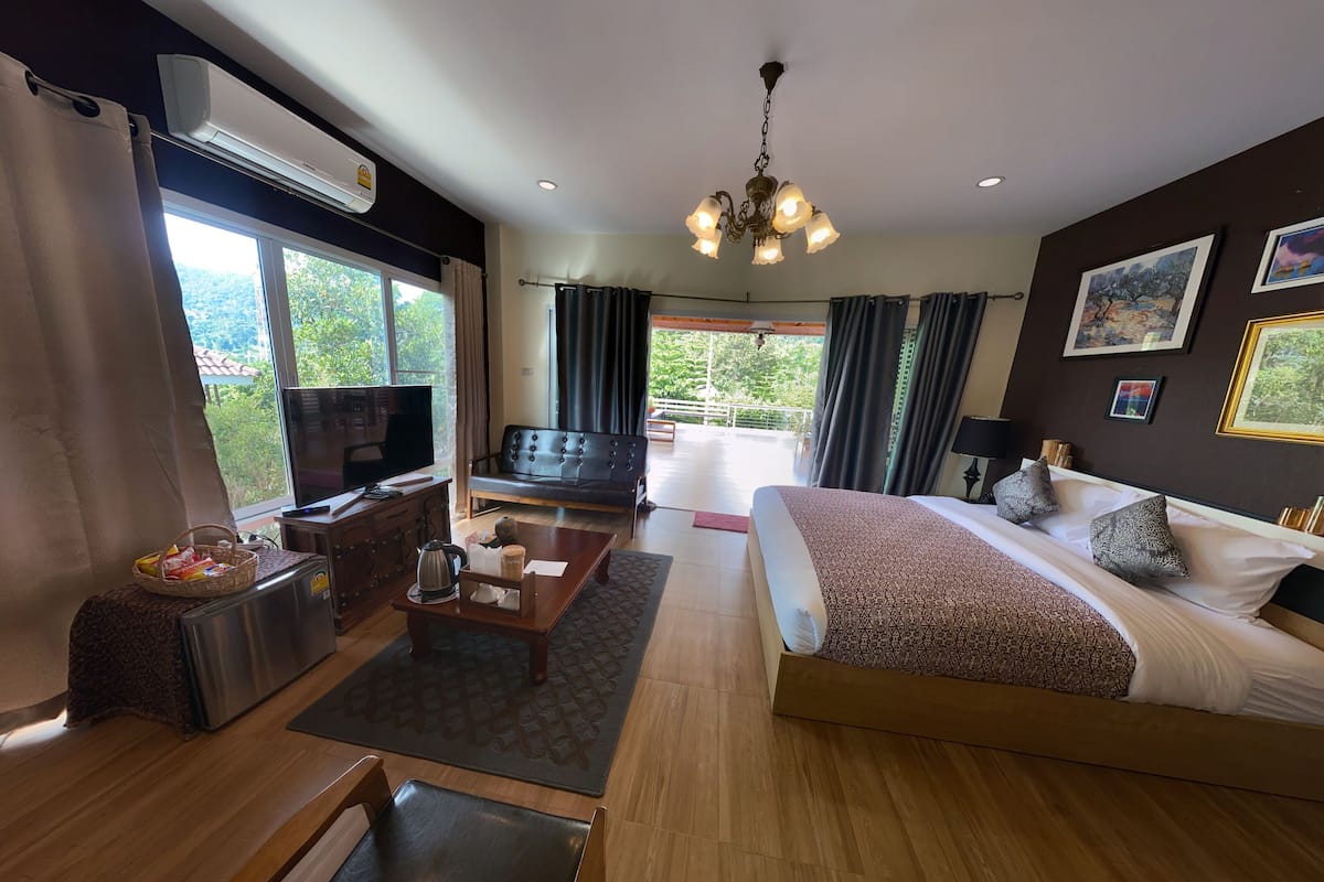 A modern hotel room with a large bed, a sofa, a TV, and a balcony with curtains.