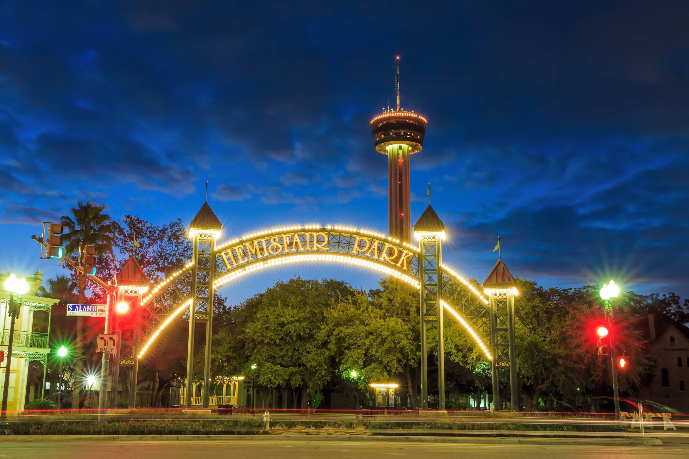 A nighttime view of a park entrance with illuminated arches and a tower.