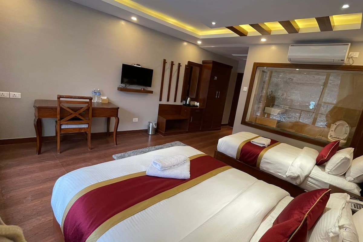 Habitación de hotel con dos camas, un escritorio, un televisor y una ventana con vistas.